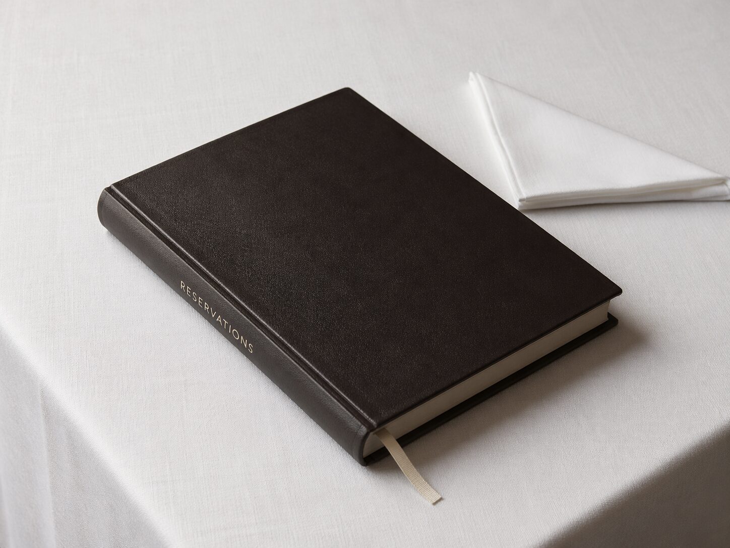 A single leather-bound reservation book closed on pressed white linen — the artifact through which every VVIP passage is scheduled and tracked